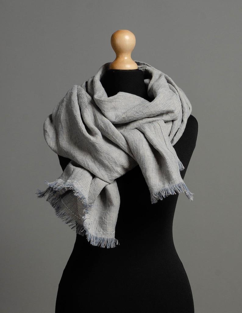 May include: A gray and white striped scarf with frayed edges, draped around a black mannequin.
