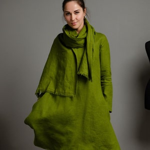 May include: A woman wearing a green linen dress with a matching green linen scarf. The dress has a loose fit and a slightly flared hem.