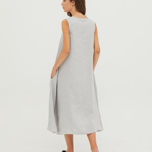 May include: A light gray sleeveless linen dress with a scoop neck and pockets. The dress has a flowy, A-line silhouette.