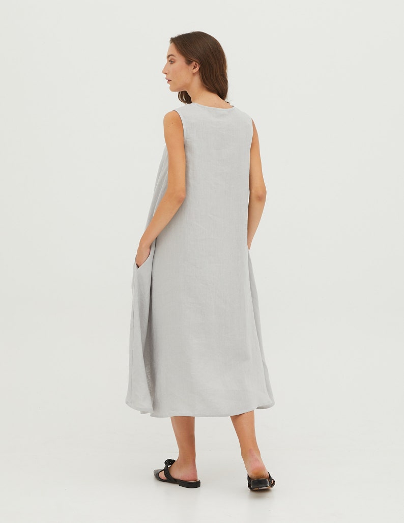 May include: A light gray sleeveless linen dress with a scoop neck and pockets. The dress has a flowy, A-line silhouette.