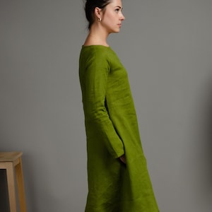 May include: A woman wearing a long-sleeved, green linen dress with a scoop neck.