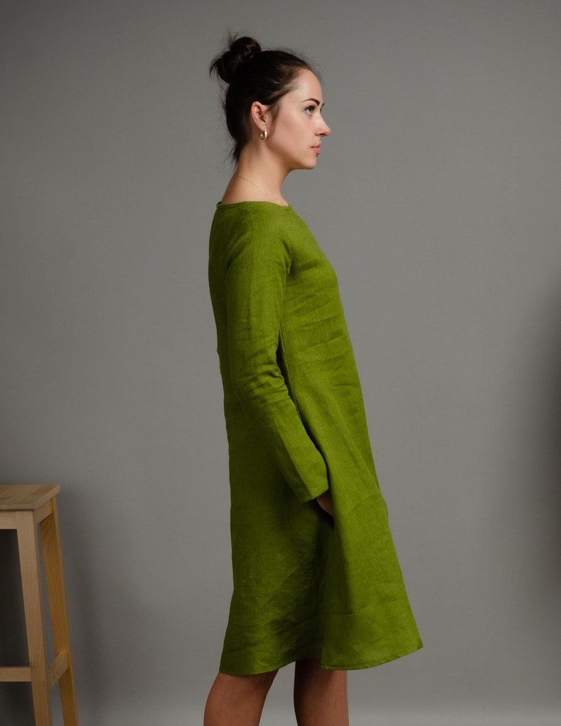 May include: A woman wearing a long-sleeved, green linen dress with a scoop neck.