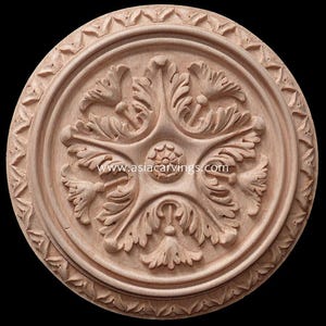 May include: A round, wooden, decorative rosette with a carved floral design. The rosette has a raised center with a smaller floral design. The rosette is surrounded by a border of carved leaves.