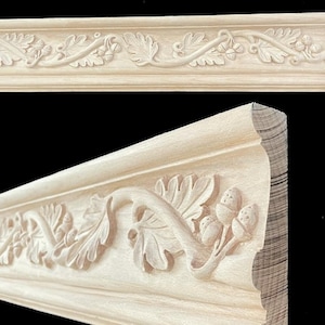 May include: Close-up of a decorative wooden molding with a carved design. The molding features a repeating pattern of leaves, acorns, and vines. The wood is a light, natural color, and the carving is detailed.