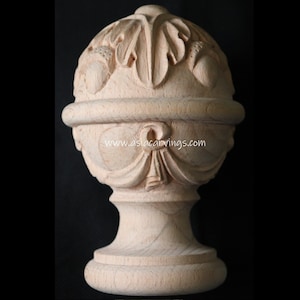May include: A wooden finial with a round top and a base. The top is carved with leaves and acorns. The base is smooth and has a slight curve. The finial is unpainted and has a natural wood color. www.aslacarvings.com