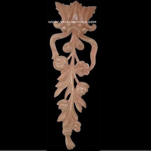 May include: A carved wooden decorative element with a floral and leaf design. The element is a light brown colour and features intricate details, including flowers, leaves, and a ribbon-like shape. The website address www.asiacarvings.com is visible.
