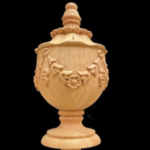 May include: A wooden finial with intricate carvings in a light brown color. The finial has a bulbous top with a decorative design and a base with a fluted design.