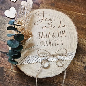 Puede incluir: Caja de madera para anillos con una base de rodaja de madera rústica, decorada con flores secas, vegetación y una cinta de encaje. La caja está inscrita con el texto "Sí, lo hacemos Julia & Tim 24.04.2024".