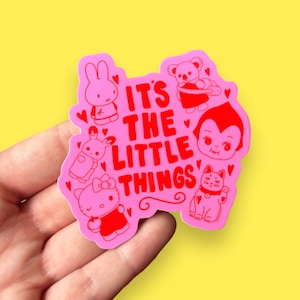 May include: Pink sticker with the text "It's the little things" in red. The sticker features various cartoon characters including a bunny, a koala, a vampire, a cat, and Hello Kitty.