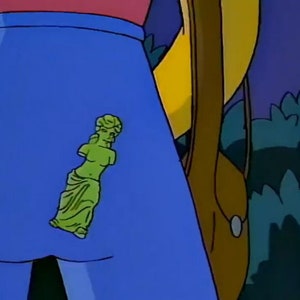 Puede incluir: Un par de pantalones vaqueros azules con una estatua de mujer de pl&aacute;stico verde unida al bolsillo trasero.