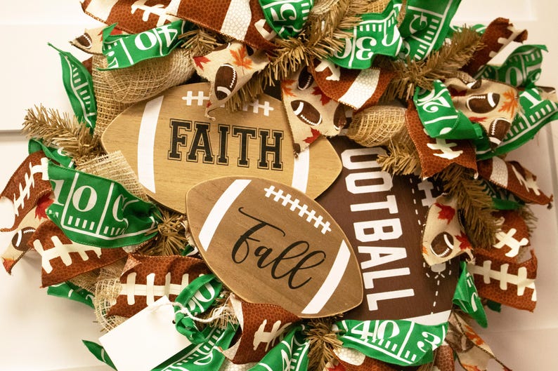 Op de afbeelding: Een bruine en groene voetbal-krans met jute, linten en twee houten voetbalborden met de tekst "FAITH" en "fall".