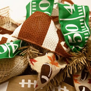 Op de afbeelding: Een bruine, witte en groene voetbal-krans met jute, herfstbladeren en een voetbalpatroon. De krans is versierd met linten waarop "50" en "10" staat.