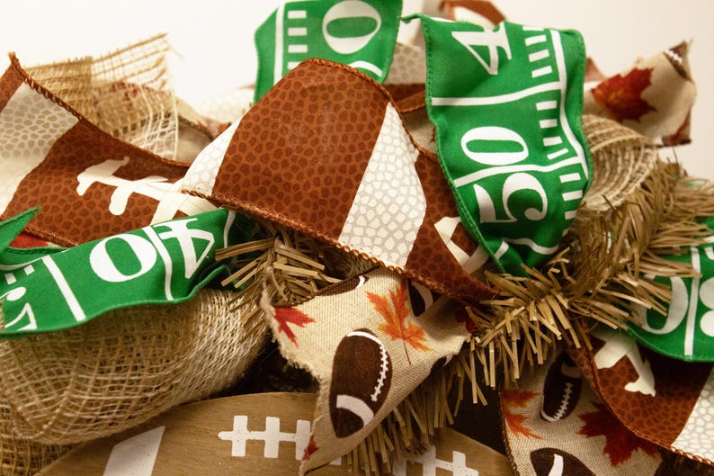 Op de afbeelding: Een bruine, witte en groene voetbal-krans met jute, herfstbladeren en een voetbalpatroon. De krans is versierd met linten waarop "50" en "10" staat.