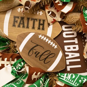 Op de afbeelding: Een bruine en groene voetbal-krans met jute, linten en houten borden met de tekst "Faith" en "Fall".