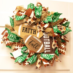 Op de afbeelding: Een bruine en groene voetbalthema krans met jute, lint en houten voetballen met de woorden "Faith" en "Fall" erop.