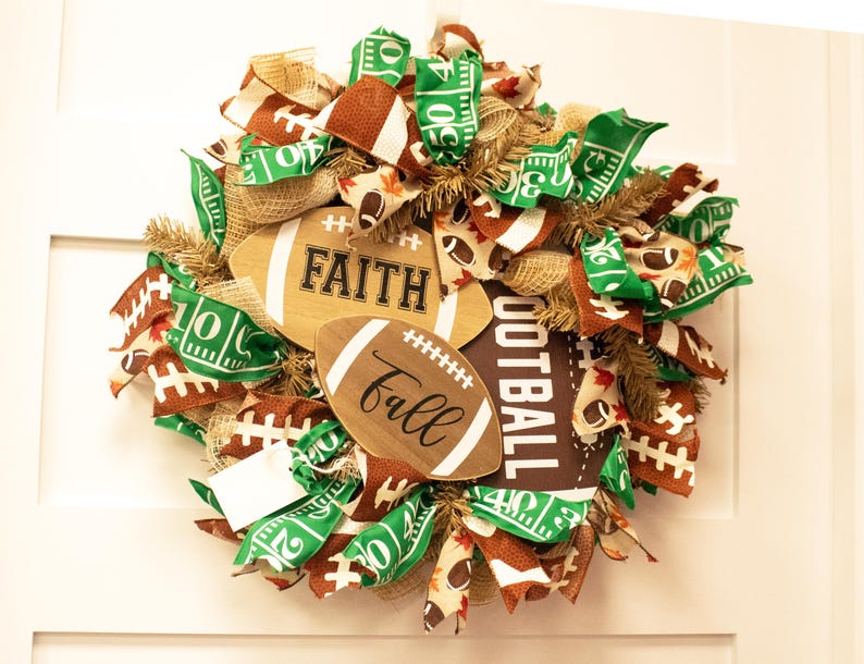 Op de afbeelding: Een bruine en groene voetbalthema krans met jute, lint en houten voetballen met de woorden "Faith" en "Fall" erop.