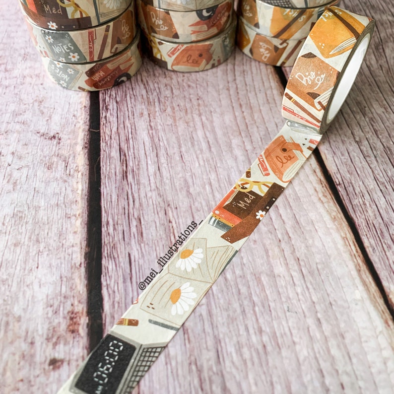 May include: Decorative washi tape rolls with a book and daisy pattern. The tape features a digital clock display showing "06:00" and the text "Med" on the tape. The background shows more rolls of tape.