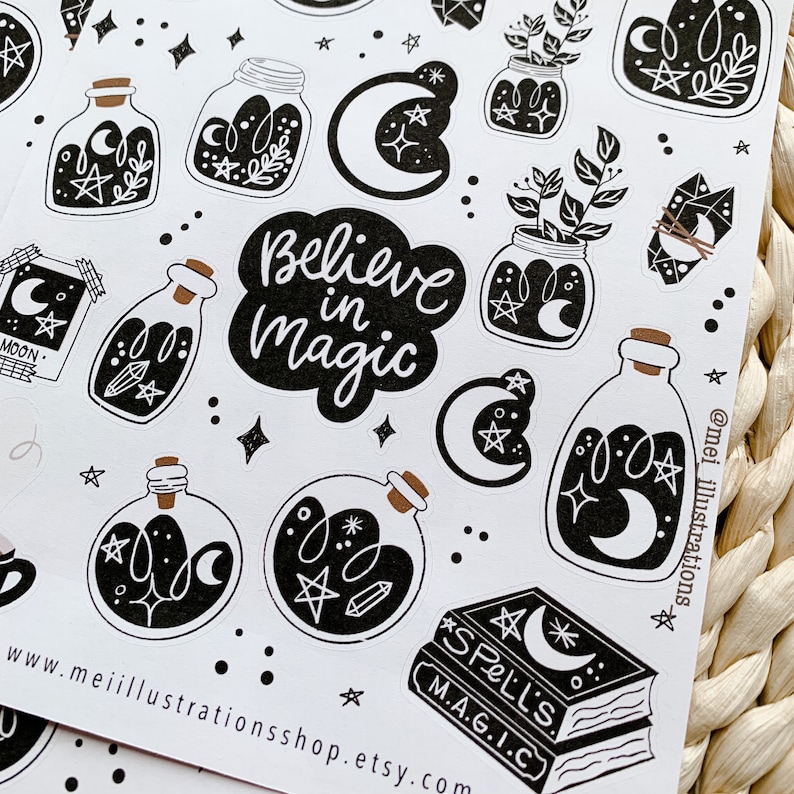 May include: A sheet of black and white stickers with a celestial theme. Designs include potion bottles, moons, stars, crystals, and the phrase "Believe in Magic." The stickers are arranged on a white background.