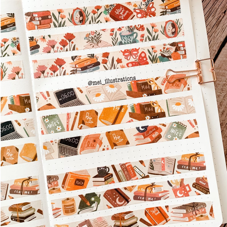 May include: Decorative washi tape rolls with various book-themed designs. The tape features illustrations of stacks of books, flowers, laptops, and the text "Read Me!" and "Notes." The color palette includes shades of brown, orange, and cream.