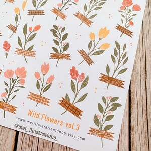 May include: Sheets of stickers featuring floral illustrations. The stickers showcase various wildflowers in shades of peach, orange, and green, secured with decorative tape. The text "Wild Flowers vol.3" is visible.