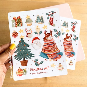 May include: A sheet of Christmas-themed stickers with festive illustrations. Designs include a decorated Christmas tree, Santa Claus, ornaments, and a girl wrapped in a blanket. The text "Christmas vol.5" is also present.