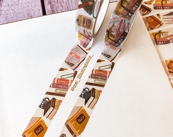 May include: Two rolls of decorative washi tape with a book theme. The tape features illustrations of books, pencils, coffee mugs, and the word "Photo". The tape is in shades of brown, orange, and cream, with some text that reads "Read me!" and "Space".