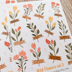 May include: Sheets of stickers featuring floral illustrations in shades of peach, yellow, and green. The flowers are affixed with brown tape. The text "Wild Flowers vol. 3" and a shop URL are visible.