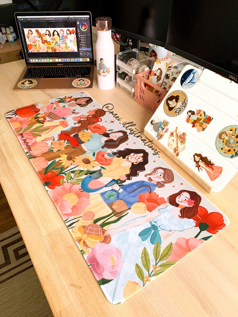 May include: A colorful desk setup featuring a laptop, water bottle, and a large mousepad. The mousepad displays an illustration of several women surrounded by flowers. The water bottle and laptop have matching illustrations. The text "@mei_illustrations" is visible.