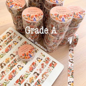 May include: A collection of washi tape rolls featuring a floral and girl illustration design. The rolls are labelled "Happy Girls" and "Mei illustrations". A notebook with matching tape strips and a single roll are also visible.