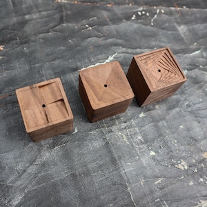 May include: Three wooden cubes with different geometric patterns carved into their surfaces. Each cube has a small hole in the center of the top.
