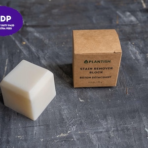May include: A solid, off-white, cube-shaped stain remover block next to its square, light brown cardboard packaging. The box features the text PLANTISH, STAIN REMOVER BLOCK, BÂTON DÉTACHANT, and 2.8 oz / 79 g printed in black ink on the front.
