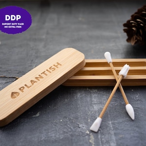 May include: A light brown bamboo storage case with a sliding lid engraved with the word PLANTISH and a leaf icon. Two reusable swabs with bamboo handles and white silicone tips are positioned in front of the open case, one with a textured end.