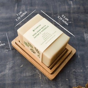 Pode incluir: Uma barra retangular de sab&atilde;o para lavar lou&ccedil;a em um prato de madeira. O sab&atilde;o &eacute; etiquetado como "PLANTISH DISH SOAP BRICK SAVON A VAISSELLE" e lista os ingredientes: "Vegano, &Aacute;gua, Azeite de oliva, &Oacute;leo de palma, Quinoa, Fragr&acirc;ncia, Mel". O sab&atilde;o mede 7 cm por 9,5 cm por 6 cm.