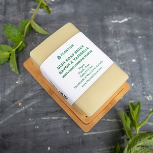 Pode incluir: Uma pastilha de sab&atilde;o para lavar lou&ccedil;a verde e branca com o texto "PLANTISH DISH SOAP BRICK SAVON &Agrave; VAISSELLE MINTY MINTI AMENTHE FRAICHE Vegan Plastic-free Palm Oil-free Handmade in Vancouver, Canada www.PlantishFuture.com" no r&oacute;tulo. A pastilha de sab&atilde;o est&aacute; sobre um saboneteira de madeira.