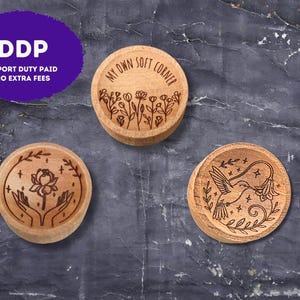 May include: Three round wooden trinket dishes with laser-engraved designs. One features a field of wildflowers and the text "MY OWN SOFT CORNER," another shows hands holding a lotus flower, and the third depicts a hummingbird near a flower.