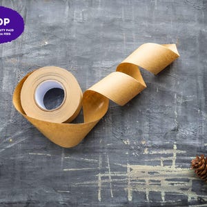 May include: A roll of light brown adhesive paper tape with a white inner core, partially unrolled to show a curved, flowing strip of the material, positioned near two brown pine cones on a dark, textured surface with a purple DDP label.