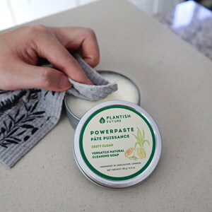May include: A round metal tin of Plantish Future Powerpaste cleaning soap with a white label featuring green text and a lemon illustration. The label reads Zesty Clean, Versatile Natural Cleaning Soap, and Net Weight 89 g / 3.5 oz.