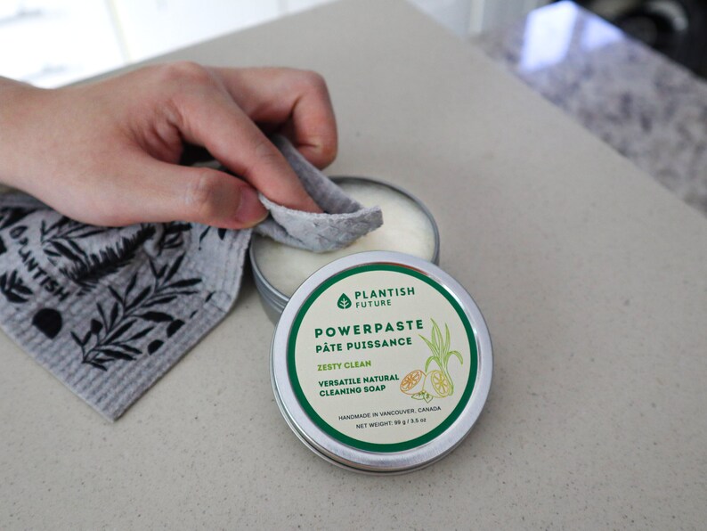 May include: A round metal tin of Plantish Future Powerpaste cleaning soap with a white label featuring green text and a lemon illustration. The label reads Zesty Clean, Versatile Natural Cleaning Soap, and Net Weight 89 g / 3.5 oz.