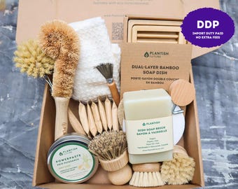 May include: A cardboard box containing eco-friendly cleaning supplies including a bamboo dish soap brick, a dual-layer bamboo soap dish, a round tin of cleaning paste, several wooden brushes with natural bristles, and a white textured cloth.