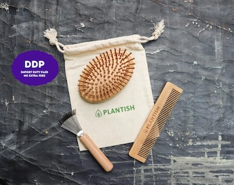 May include: An oval wooden hairbrush with rounded bristles, a rectangular wooden comb, and a small metal cleaning tool with a wooden handle, all arranged on a beige drawstring pouch featuring the green text and leaf logo of PLANTISH.