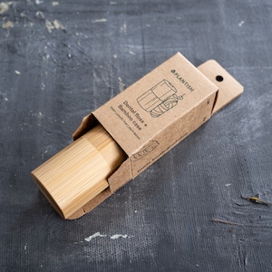 May include: A cylindrical bamboo dental floss case partially inside a brown cardboard box. The packaging features the text PLANTISH, Dental floss + Bamboo case, vegan | plastic-free | plant-based, and 100% biodegradable with a line art illustration.