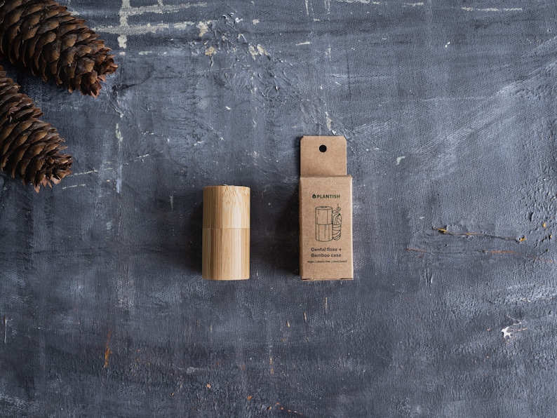 May include: A cylindrical bamboo dental floss case and its matching brown cardboard packaging box. The box features the Plantish logo, a line drawing of the floss container, and the text Dental floss + Bamboo case, vegan, plastic-free, plant-based.