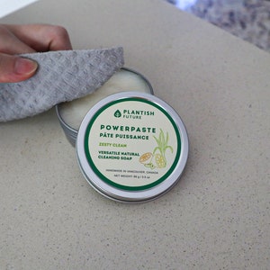 May include: A round metal tin of Plantish Future Powerpaste Zesty Clean natural cleaning soap. The label features green text, a leaf icon, and a lemon illustration. The net weight is 99 g / 3.5 oz. The tin is partially open, revealing white paste.