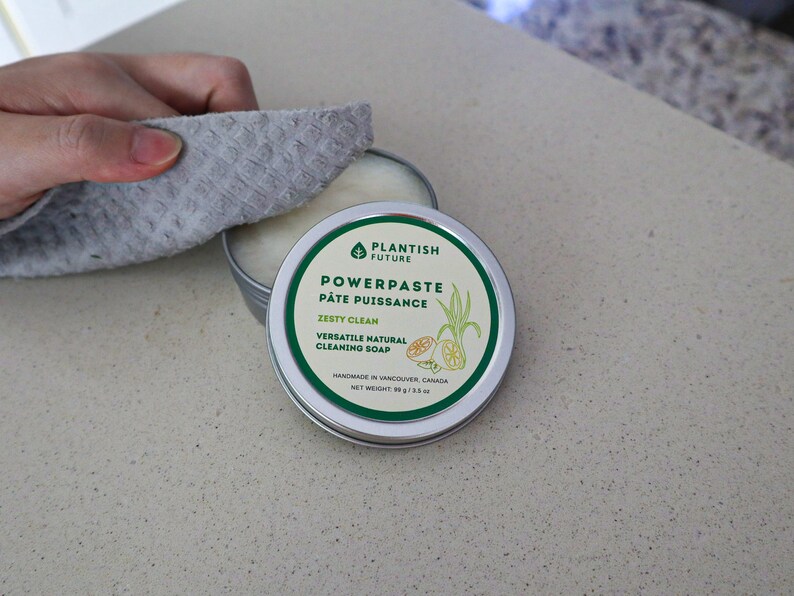 May include: A round metal tin of Plantish Future Powerpaste Zesty Clean natural cleaning soap. The label features green text, a leaf icon, and a lemon illustration. The net weight is 99 g / 3.5 oz. The tin is partially open, revealing white paste.