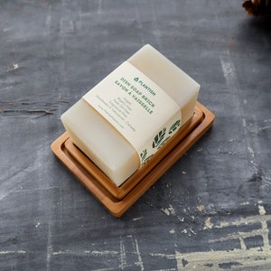 Pode incluir: Uma barra de sab&atilde;o para lavar lou&ccedil;a branca com um r&oacute;tulo verde e branco que diz "Plantish Dish Soap Brick Savon &agrave; Vaisselle Vegan Palm Oil Free Fragrance Free Made in Vancouver, Canada plantishsoap.com", sentada em um saboneteira de madeira.