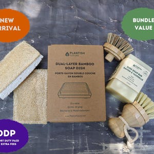 May include: A set of cleaning supplies including two rectangular loofah sponges, a brown cardboard box labeled Dual-Layer Bamboo Soap Dish, a square dish soap bar, and two round bamboo brushes with light-colored bristles and a cotton rope loop.