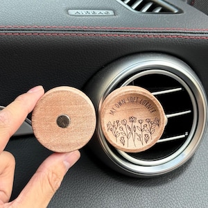 May include: Two round wooden car air fresheners. One has a magnet on the back. The other has the text "MY OWN SOFT CORNER" and a floral design etched into the wood.