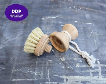 May include: A two-piece wooden dish brush with a detachable head featuring light-colored stiff bristles and a threaded screw mechanism. The handle has a concave shape and includes a white cotton rope loop attached to the side for hanging.