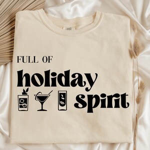 May include: A white t-shirt with black text that reads "FULL OF holiday spirit" with three cocktail drink icons.