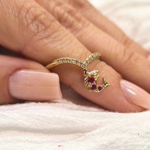 May include: Gold ring with a V-shaped band and a dangling charm of a red fish with clear stones.